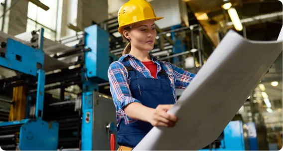 Female engineer reviewing blueprints in an industrial setting – Master of Engineering Project Management in Australia